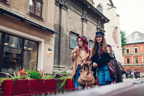 Outdoor shot of young women walking on city street. and having coffee. Happy friends talking and having fun